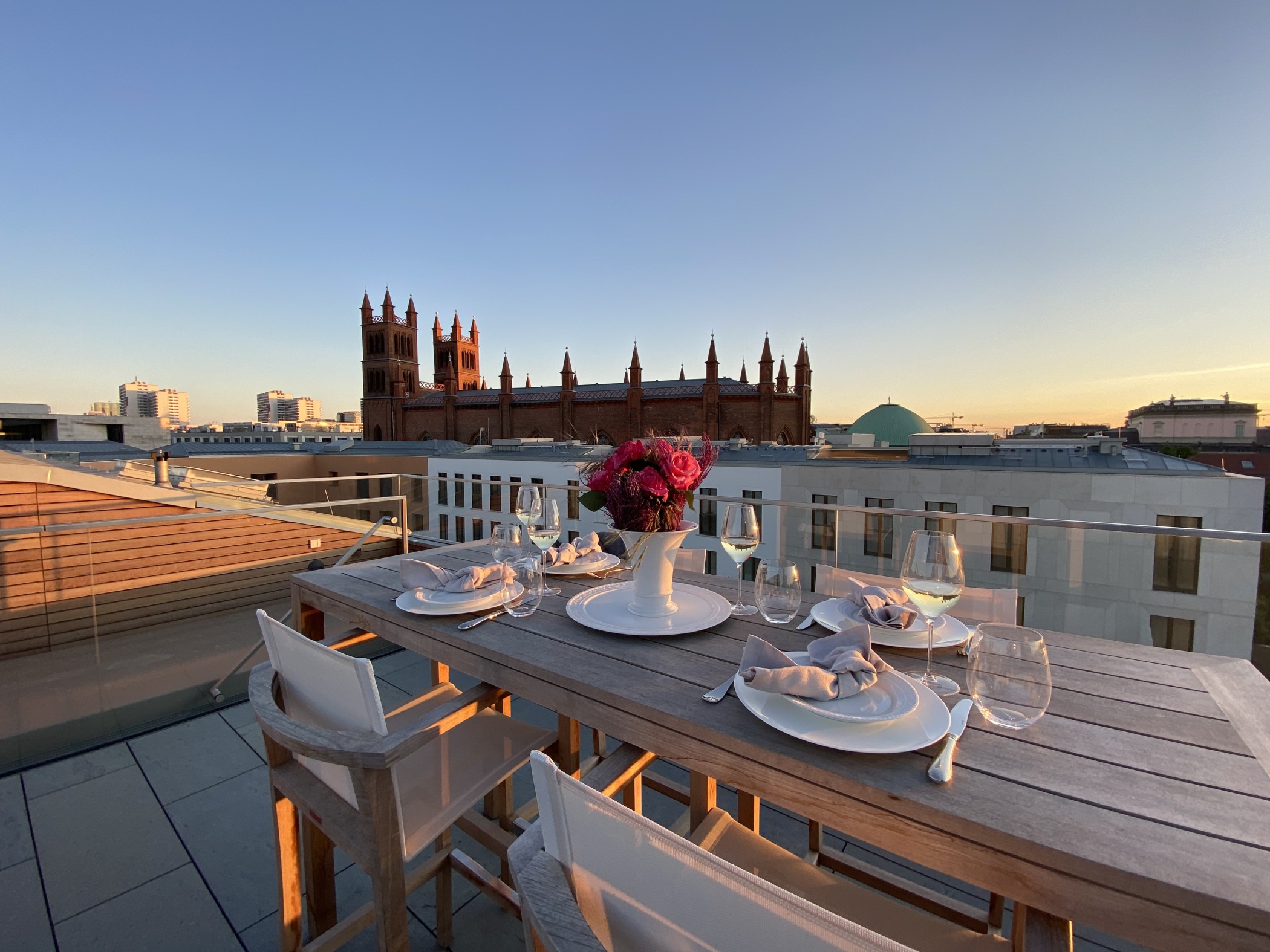 Stimmungsvolle Rooftop-Tafel bei Sonnenuntergang mit Blick auf die Friedrichswerdersche Kirche und die modernen Wohnresidenzen am Schinkelplatz in Berlin-Mitte.