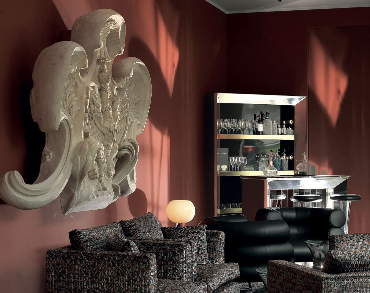 Lounge mit roter Wand, großem weißem Stuckornament, gemusterten Sofas und verspiegeltem Barschrank