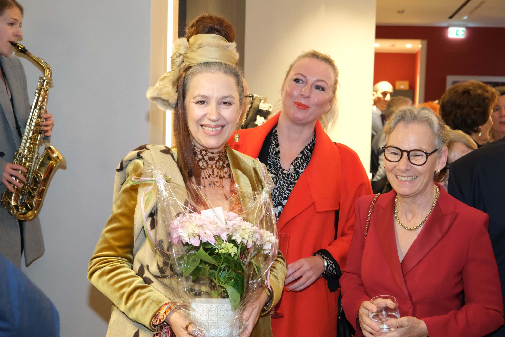 Lächelnde Gäste mit Blumenstrauß bei einem Empfang in der Lounge, links ein Saxofonist