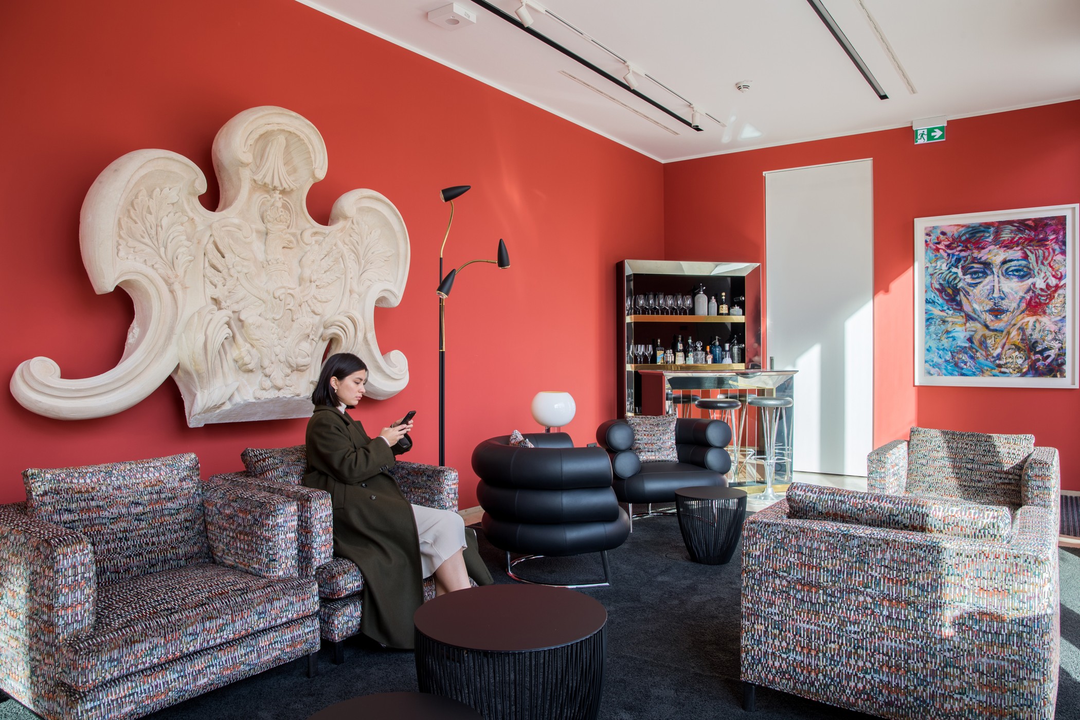 Frau mit Smartphone auf einem Sessel in der Lounge mit roter Wand, Stuckornament und Porträtgemälde