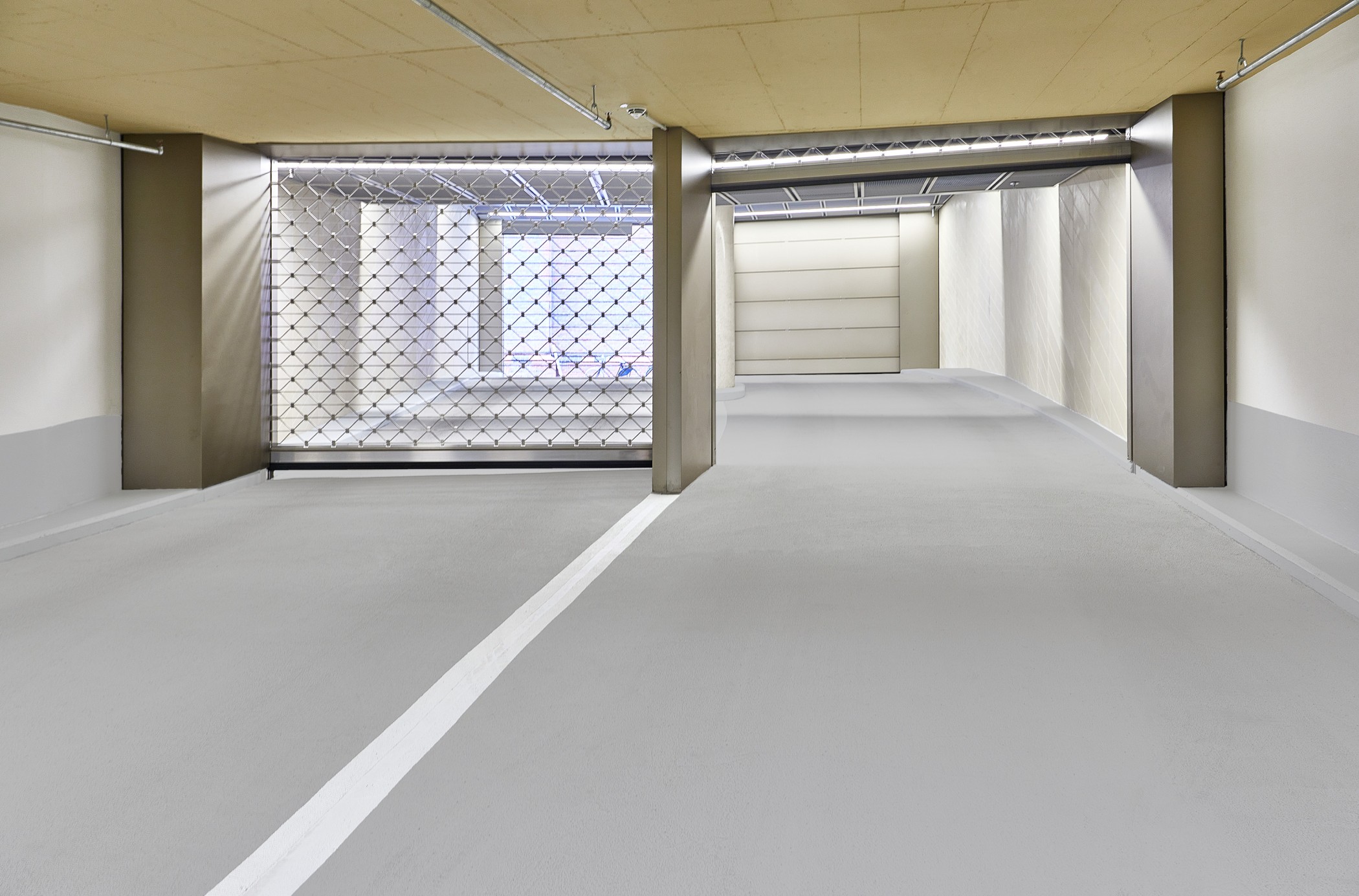 Tiefgaragenzufahrt mit Rautengitter-Tor, weißen Wänden und markierter Fahrspur
