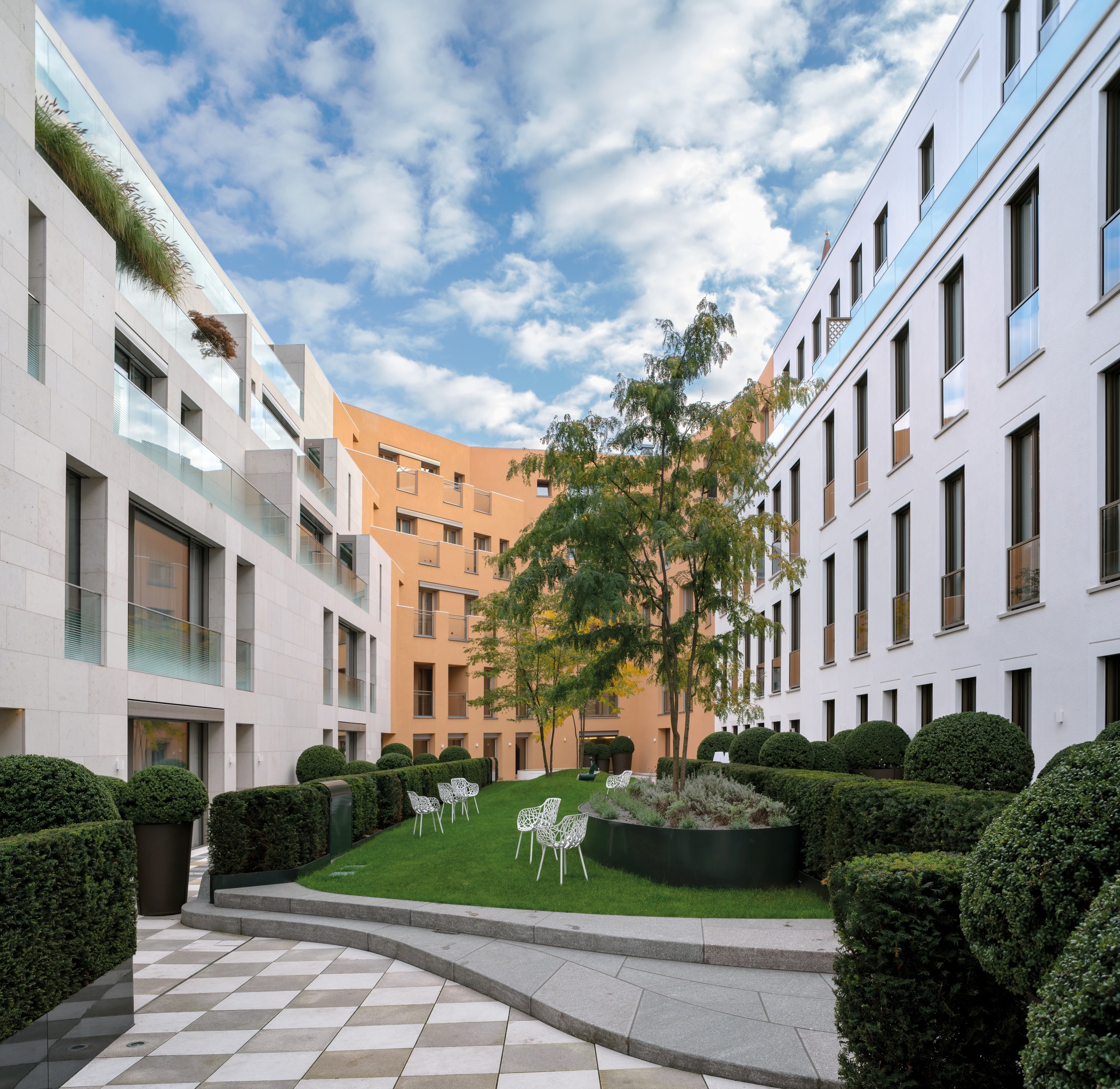 Begrünter Innenhof moderner Wohnresidenzen am Schinkelplatz in Berlin-Mitte mit gestalteter Gartenanlage und Sitzbereichen.
