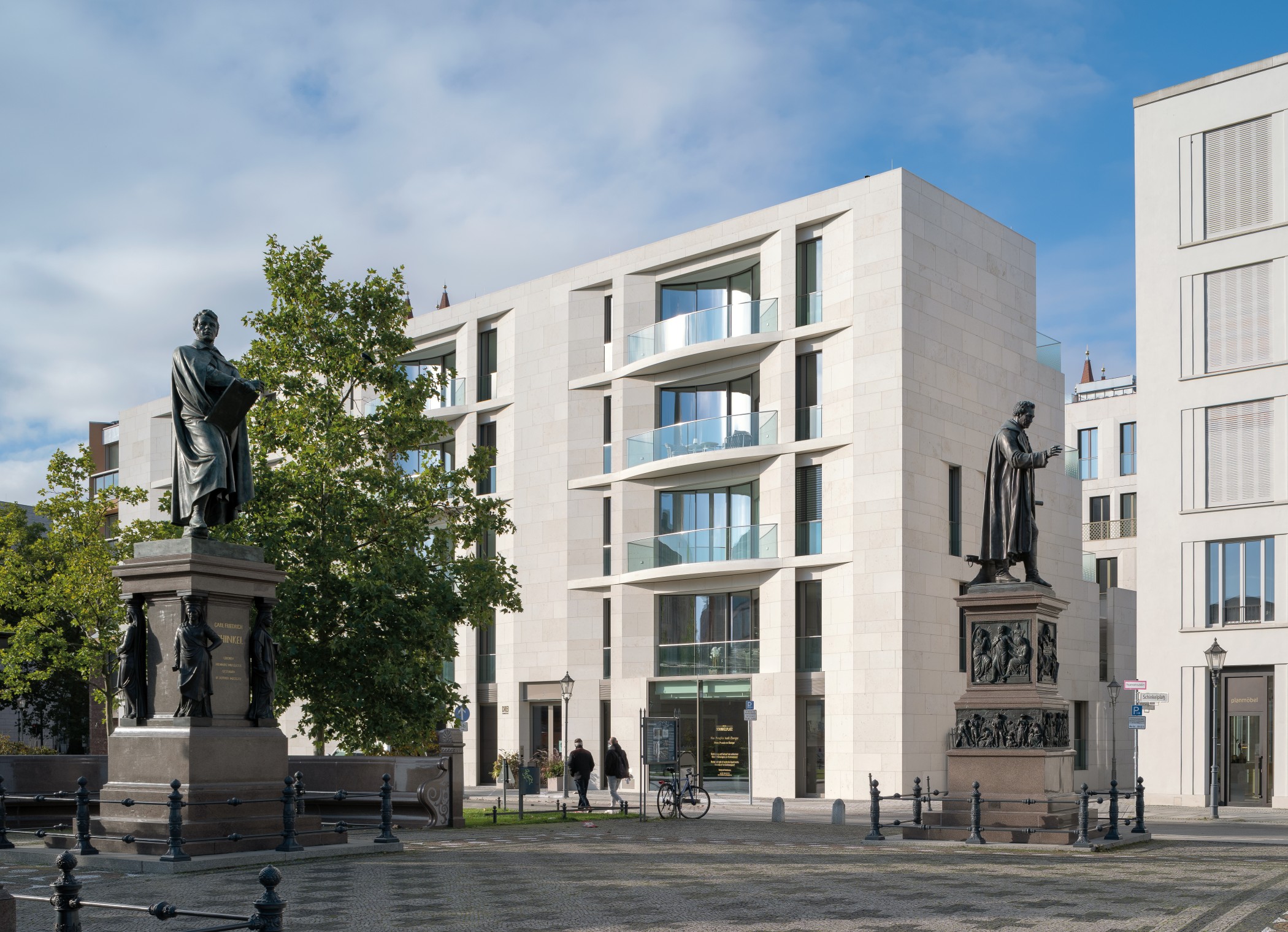 Schinkel- und Beuth-Denkmal vor einem hellen Natursteinbau mit gläsernen Balkonen am Schinkelplatz