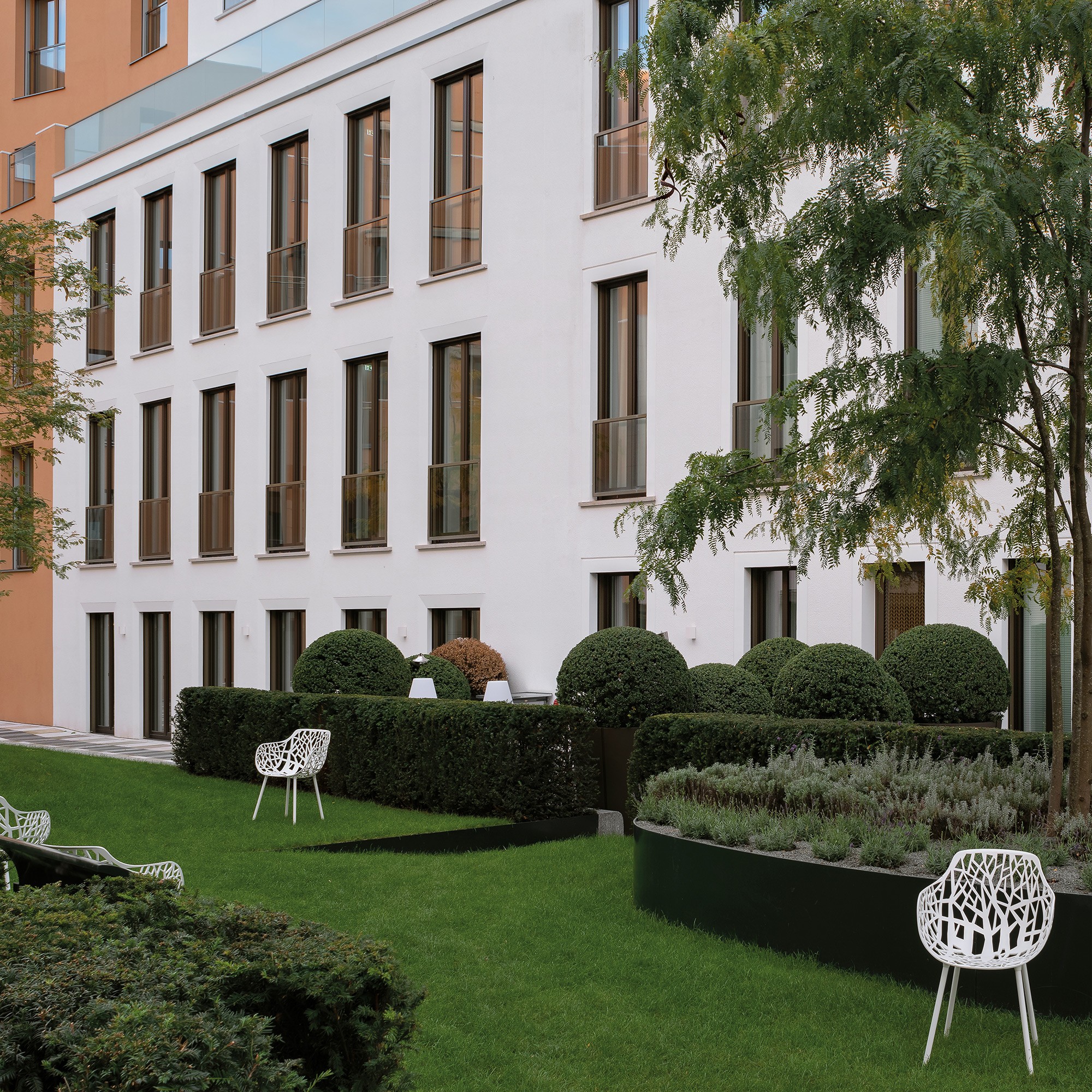 Rasenfläche im Innenhof mit weißen Gartenstühlen, Buchshecken und Lavendelbeet vor heller Fassade