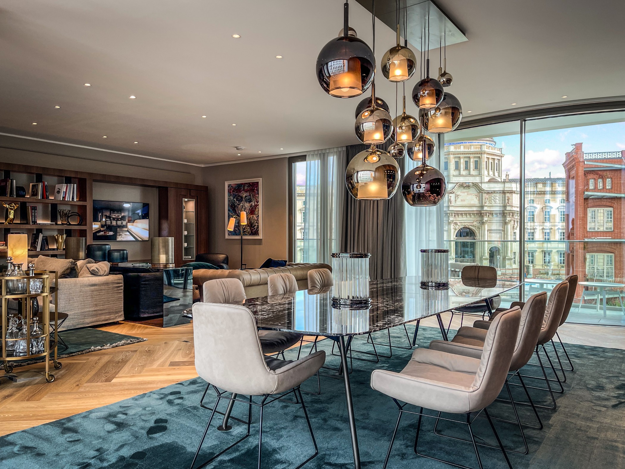 Exklusiver Wohn- und Essbereich einer Luxuswohnung am Schinkelplatz in Berlin mit großem Marmortisch, Designerleuchten und Blick auf die historische Fassade des Humboldt Forums.