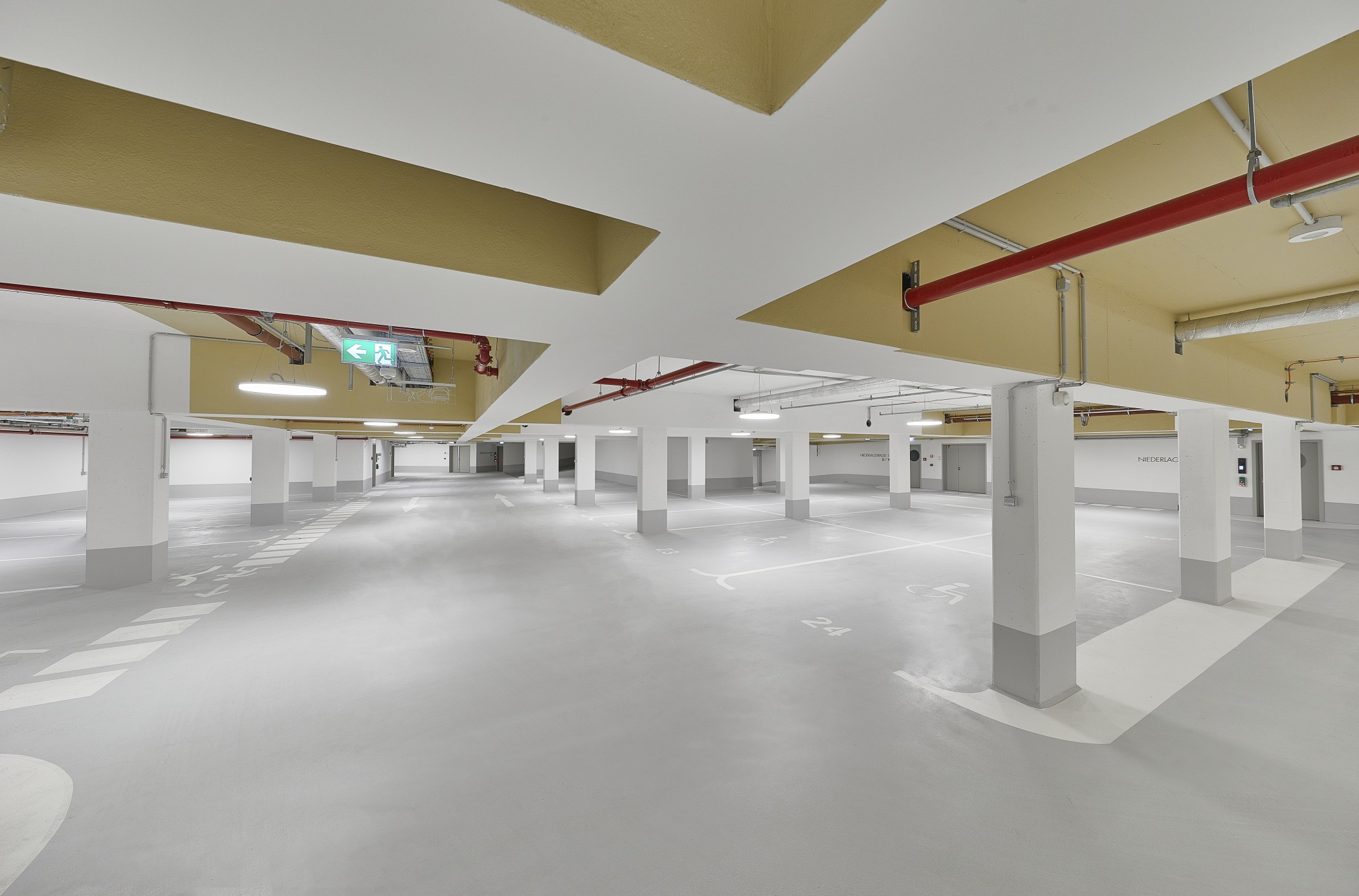 Weitläufige helle Tiefgarage mit weißen Stützen, markierten Stellplätzen und gelb abgesetzter Decke