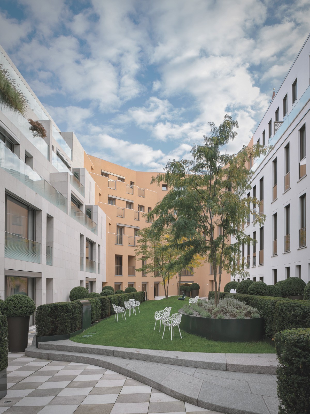 Begrünter Innenhof moderner Wohnresidenzen am Schinkelplatz in Berlin-Mitte mit gestalteter Gartenanlage und Sitzbereichen.