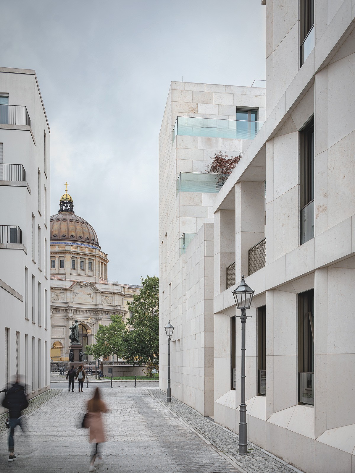 Gasse zwischen hellen Natursteinbauten mit Blick auf ein Denkmal und die Kuppel des Humboldt Forums