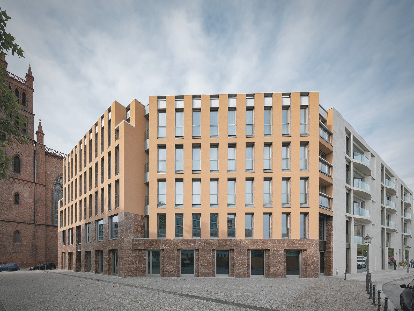 Moderne Wohnarchitektur am Schinkelplatz in Berlin-Mitte mit gelbem Fassadenbau und angrenzender historischer Friedrichswerderscher Kirche.