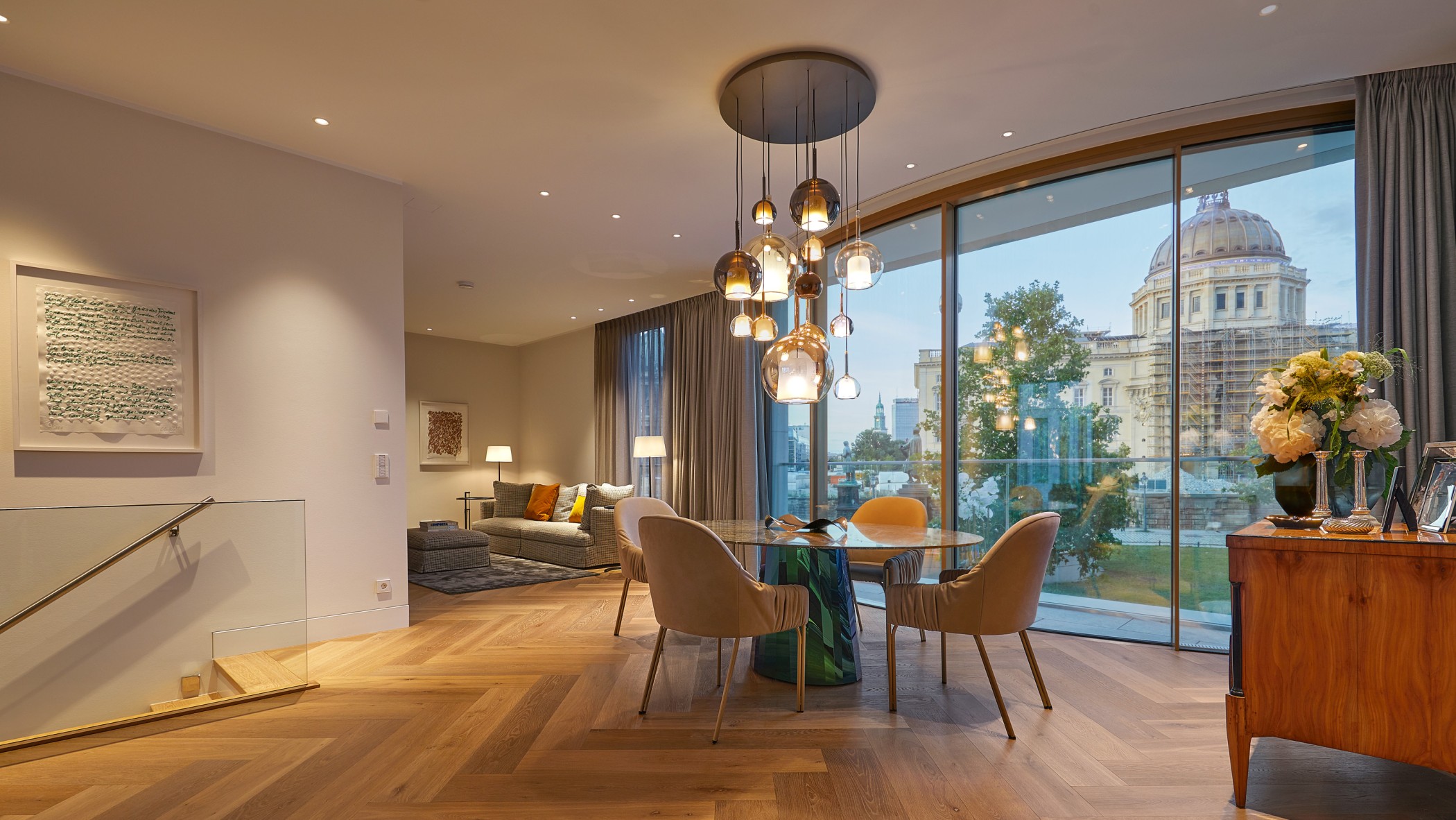 Exklusiver Wohn- und Essbereich einer Luxuswohnung am Schinkelplatz in Berlin mit großem Marmortisch, Designerleuchten und Blick auf die historische Fassade des Humboldt Forums.